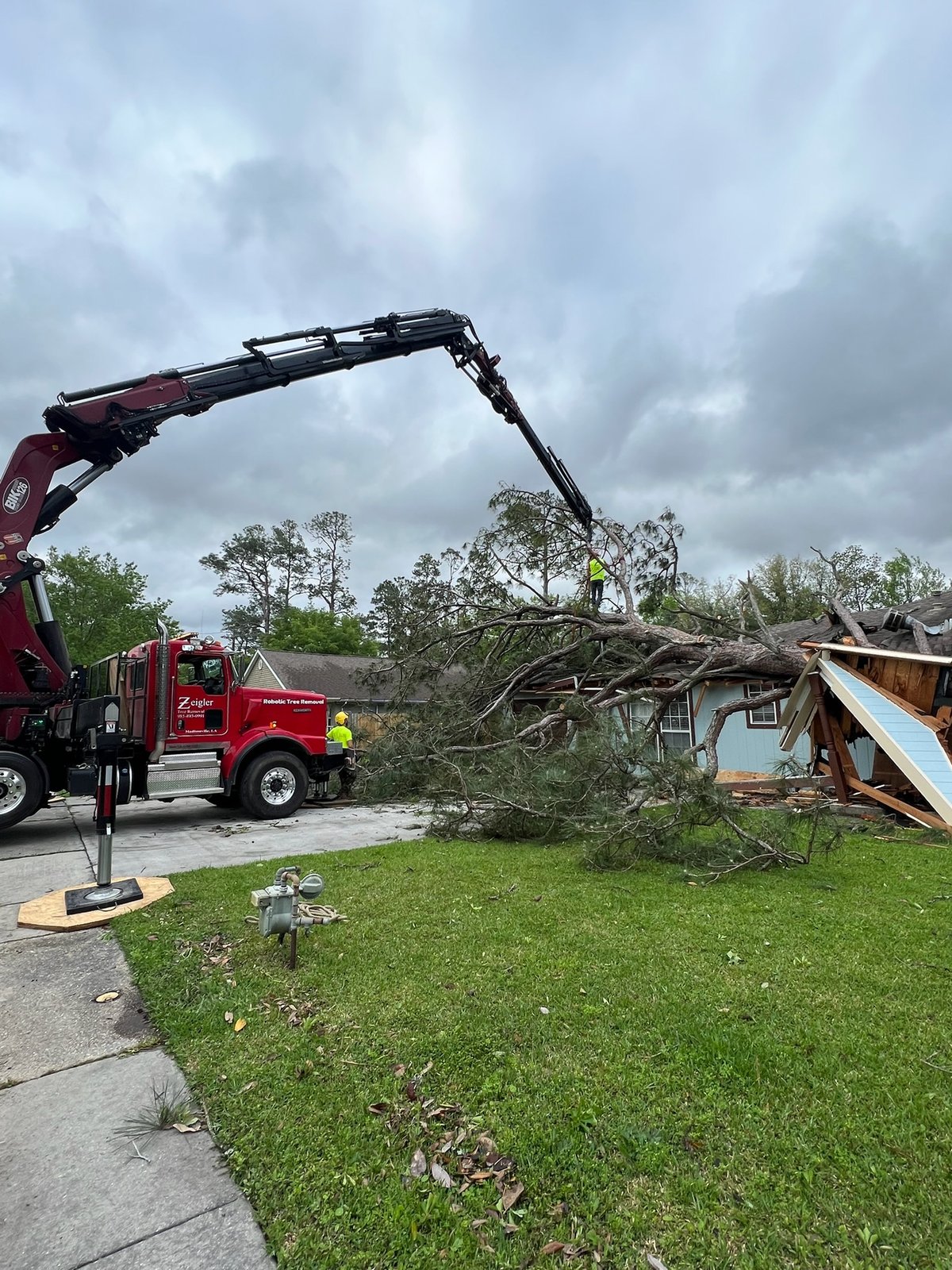 Grapple truck removing a fallen tree from a storm-damaged home