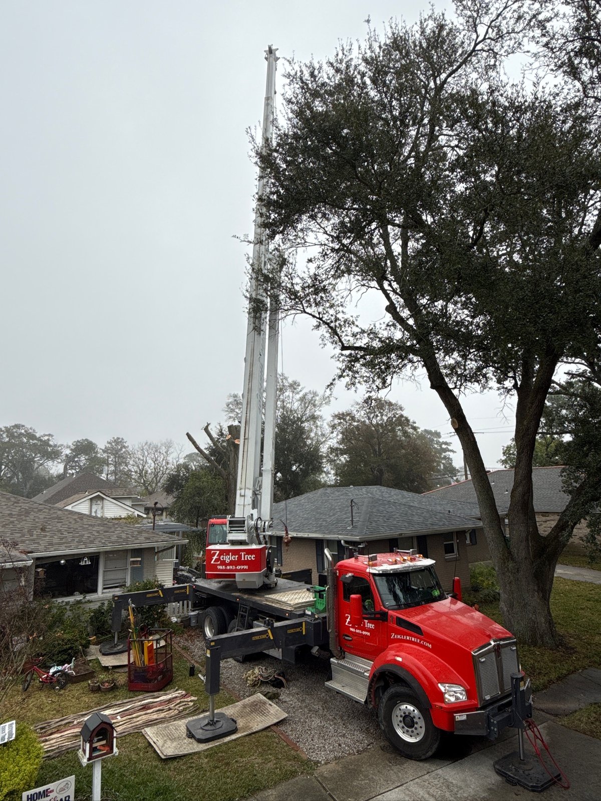 Crane truck extending high above a residential yard for a tree removal